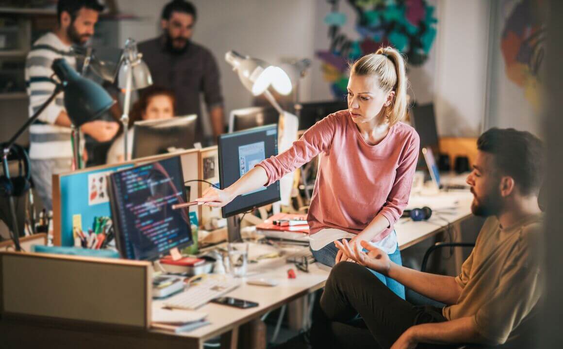 A woman sitting on her colleagues desk showing him some new analytics