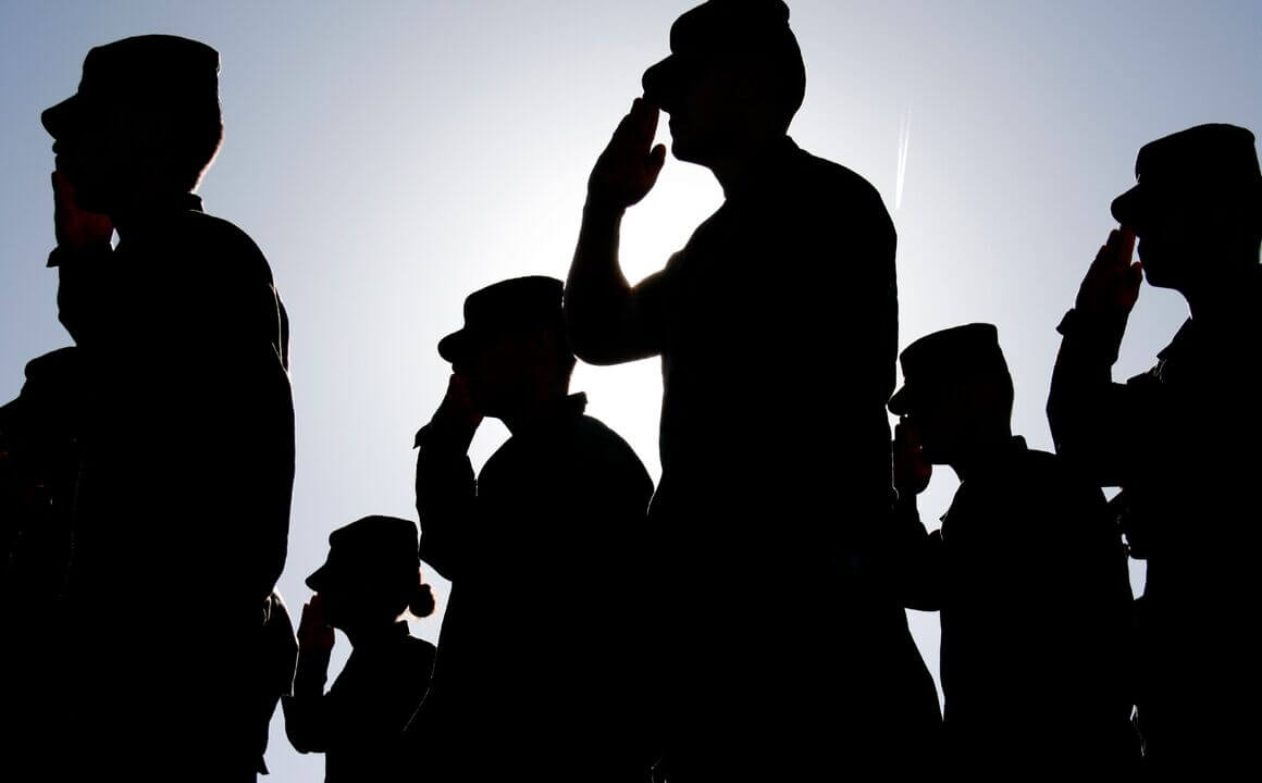 Several soldiers salute the flag at sunset during a military exercise. 