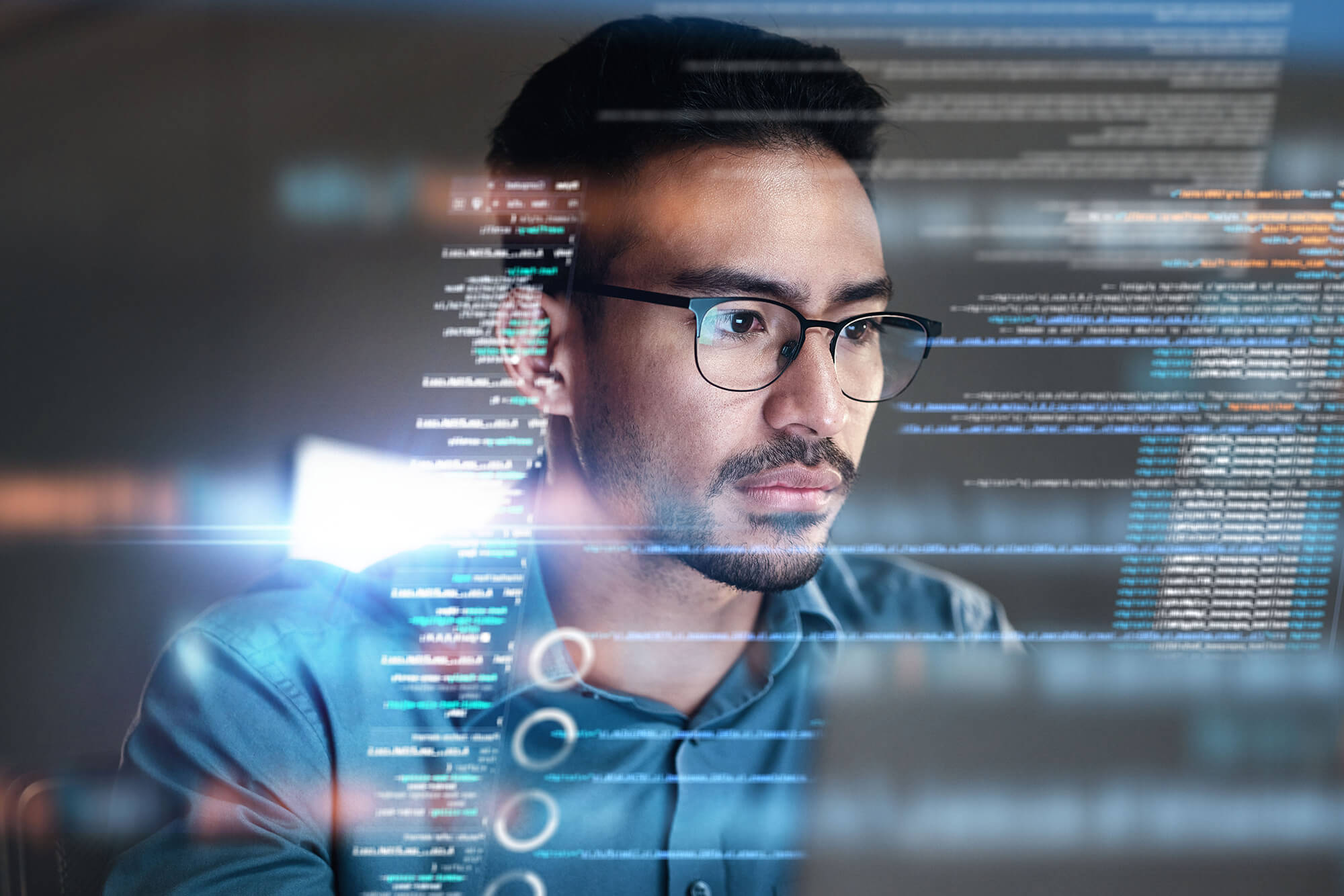 Man with glasses looking at a computer screen with data overlay surrounding him.
