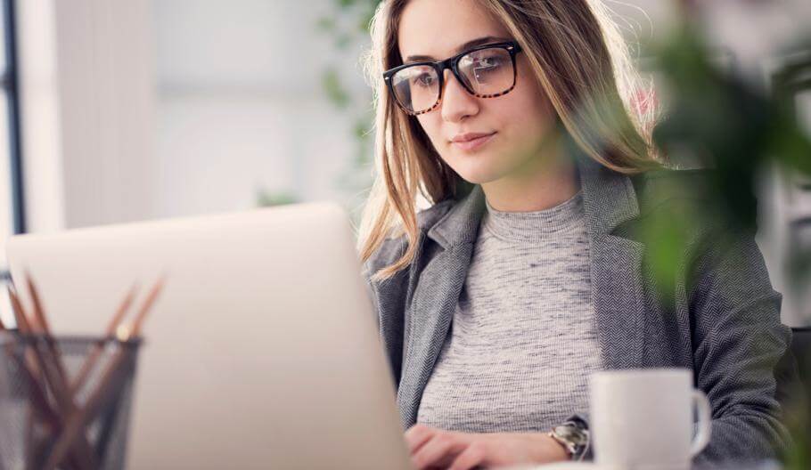 Woman wearing glasses sitting at desk working on laptop