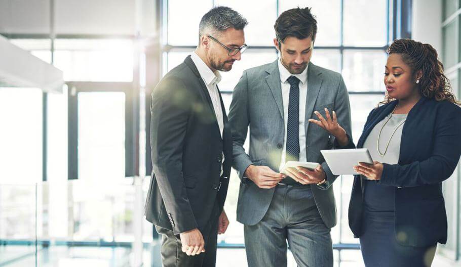 coworkers standing and meeting reviewing a tablet