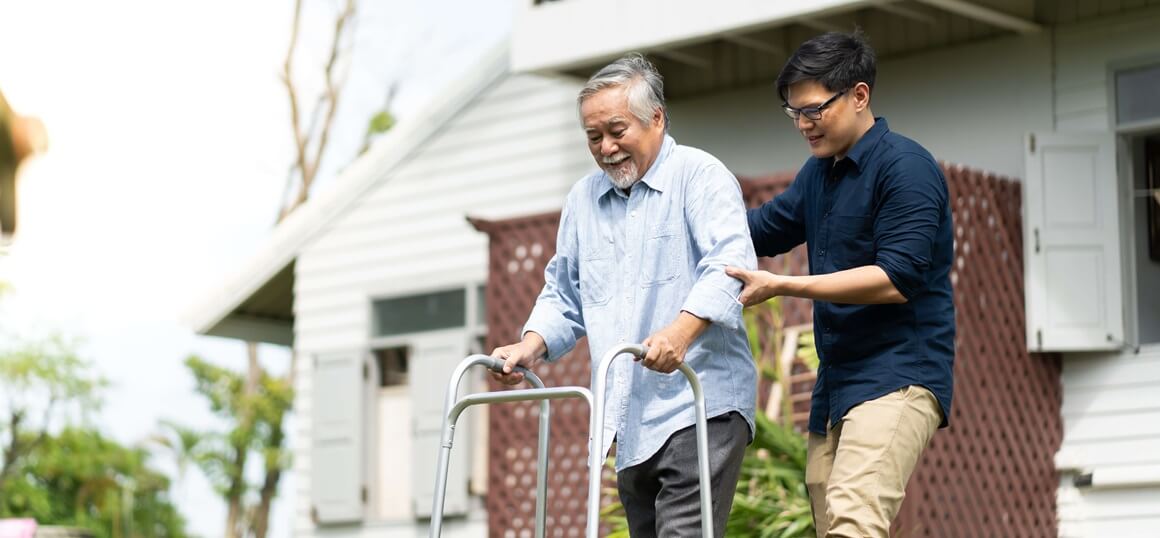Eldery man in the wheel chair beeing assited by a younger caregiver outside