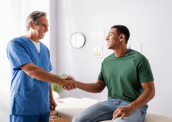 Patient shaking his doctors hand while sitting on an examination table.