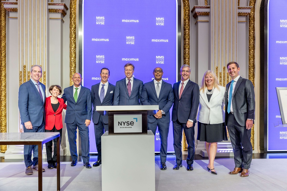 The Maximus executive team poses at the NYSE podium. Pictured (left to right): Kevin Reilly, Ilene Baylinson, Lou Shields, John Martinez, Jericho Seguin, Derrick Pledger, Bruce Caswell, Michelle Link, David Mutryn.