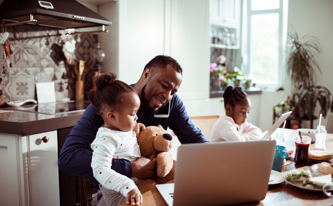 Father on phone looking at laptop with daughter on his lap.