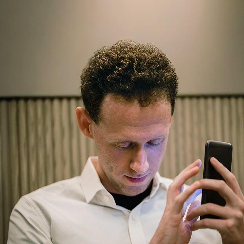 A man with a visual impairment uses a mobile device to select health insurance coverage through a government website. He holds the device with both hands in front of him, his face pointed down, and his eyes closed. 