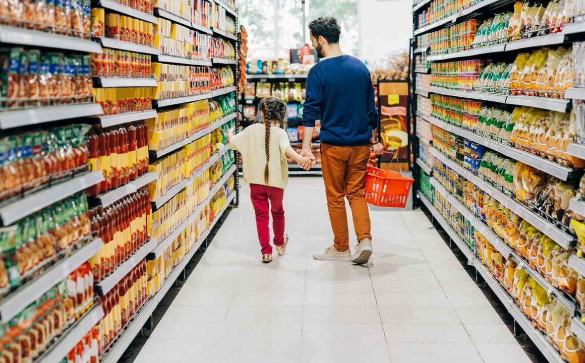 Father and daughter hold hands while they walk down a grocery store aisle to purchase food with replacement SNAP benefits.