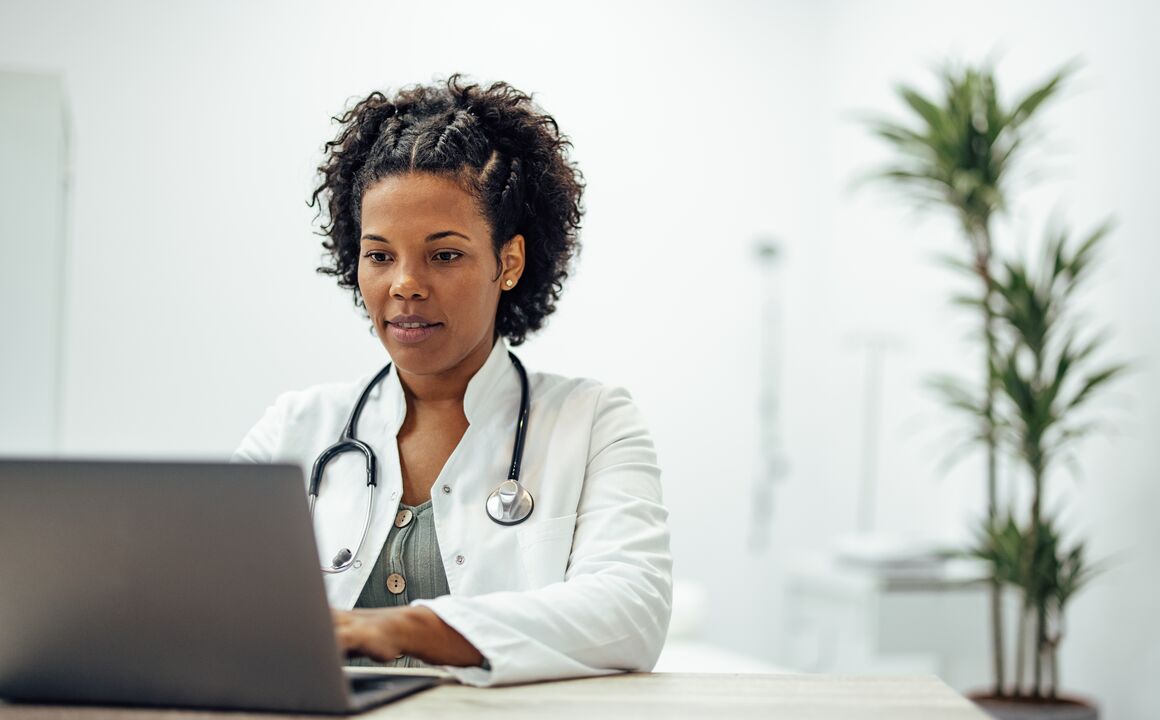 Female doctor wearing white coat and stethoscope types on laptop