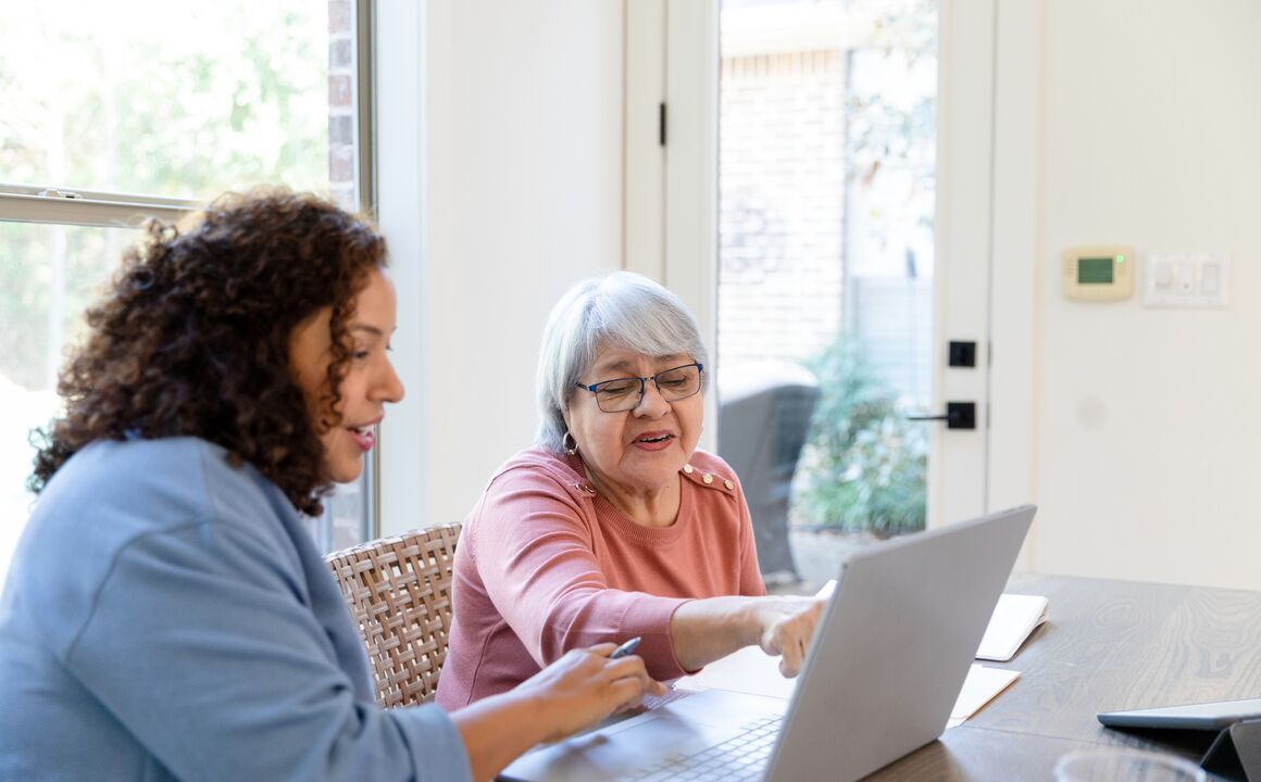 A mid adult daughter helps her senior adult mother understand a computer budgeting program.