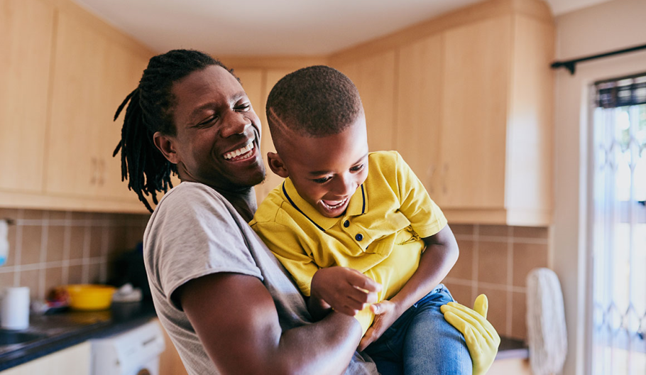 Empowered father hugs his young son while cleaning the kitchen in their home