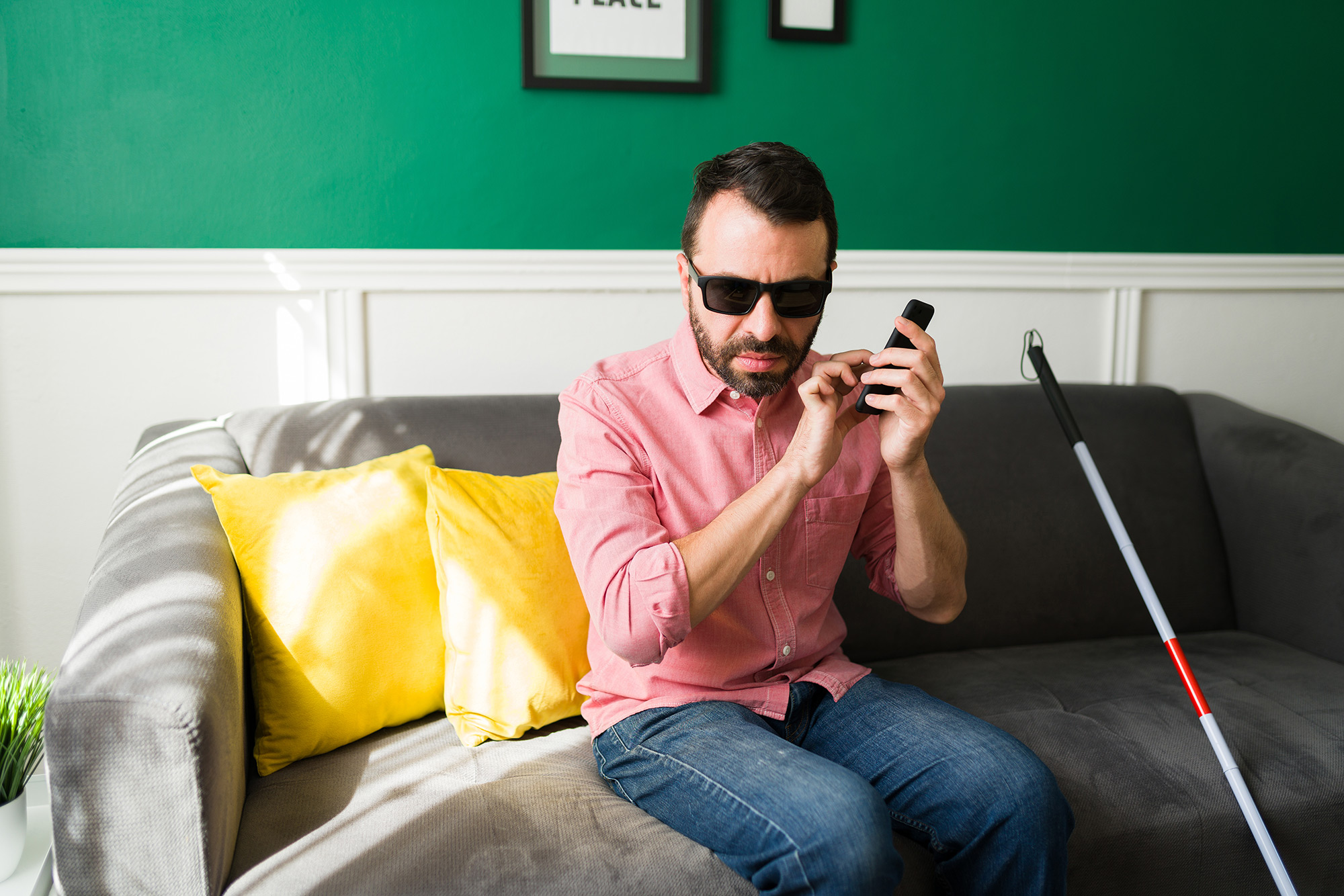 Blind man sitting on couch using phone.