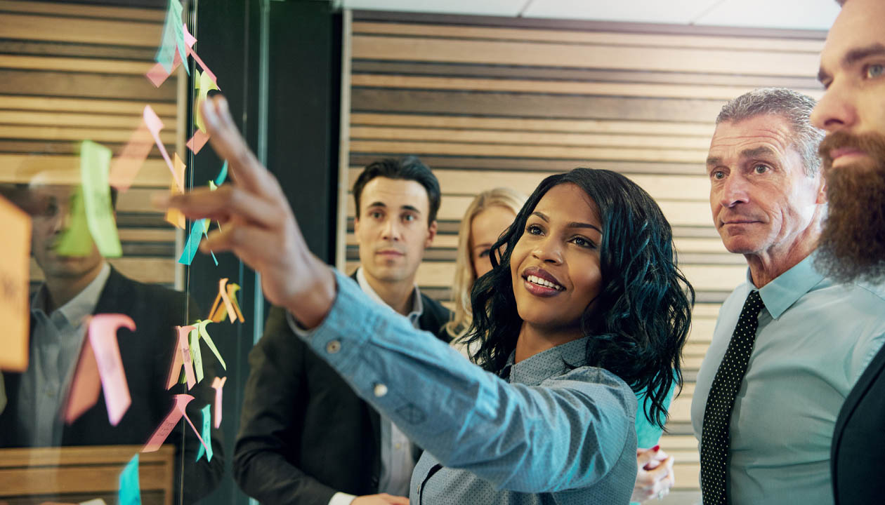 businesswoman points to sticky note while brainstorming with colleagues