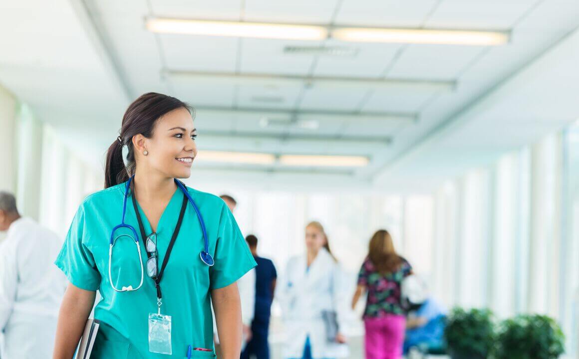 Smiling young doctor walks down hospital hallway with staff in background