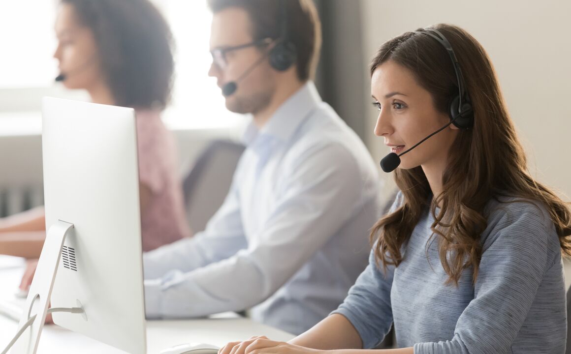 Female customer service agent speaks into headset while looking at computer screen and typing