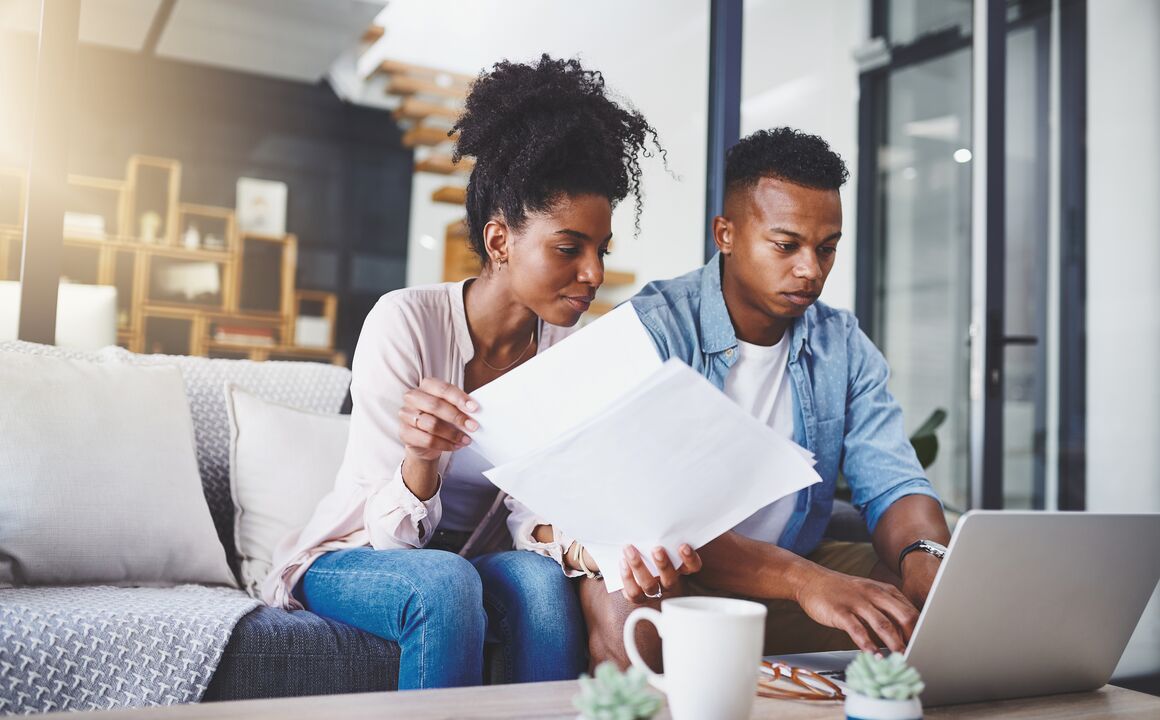 A young couple compares paperwork to a laptop screen while they enroll in health insurance through their state-based marketplace