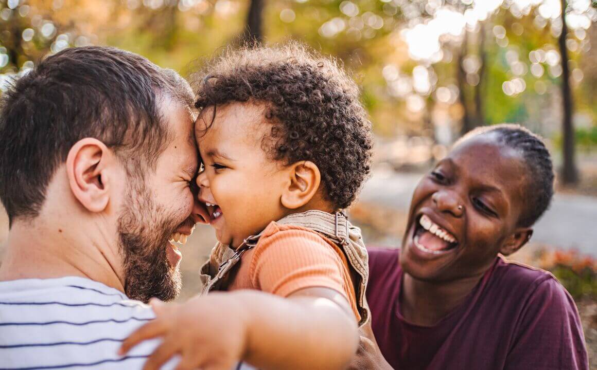 Happy noncustodial father hugs toddler son and hands to his smiling custodial mother as part of their co-parenting agreement.