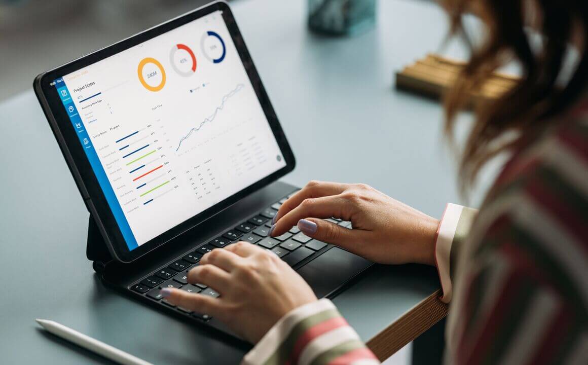 Woman in striped shirt working on tablet displaying colorful graphs and data analysis in a business environment.