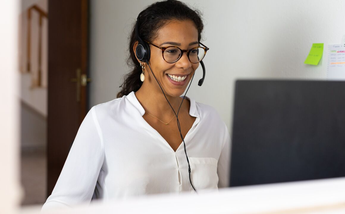 Contact center agent answers calls from her home during a surge of government customer inquiries. She is wearing a headset and smiling as she looks at her monitor.