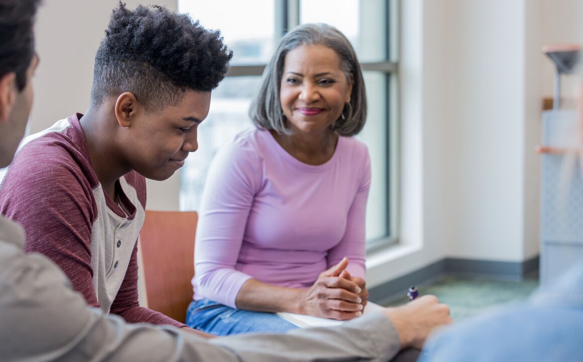 A teen boy smiles shyly and looks downward as a clinical professional conducts a Qualified Residential Treatment Program assessment to ensure his needs are met. 