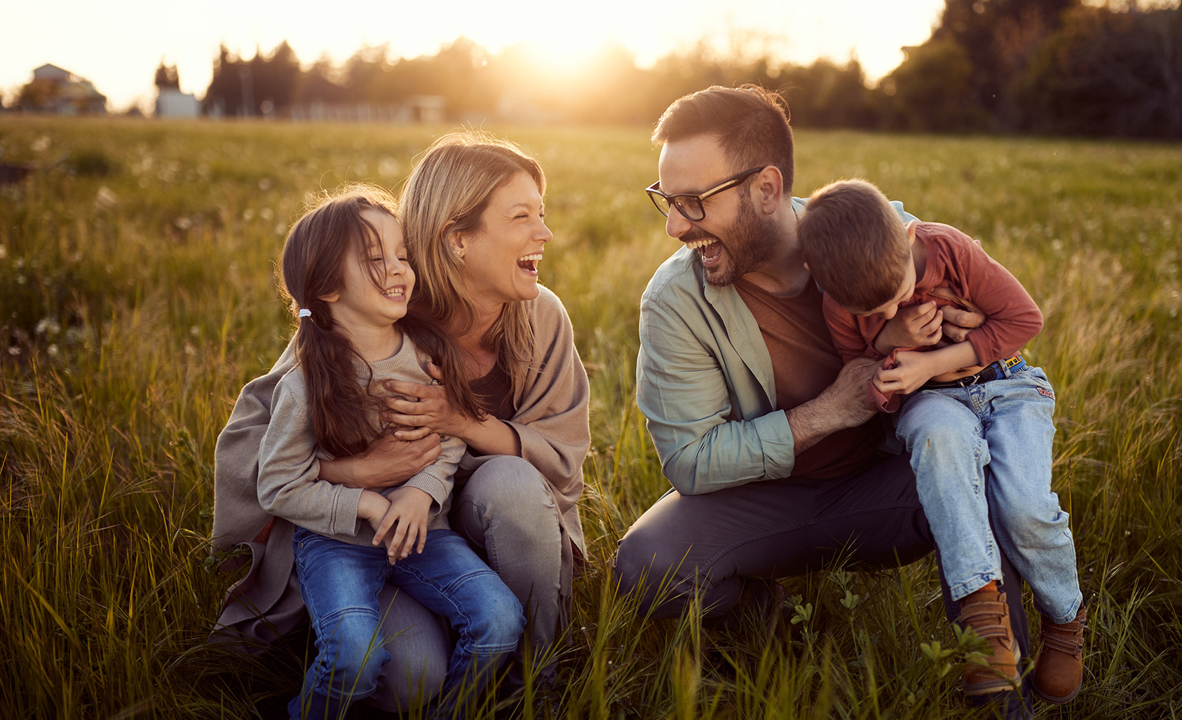 Family laughing while sitting in a field while the sun sets.