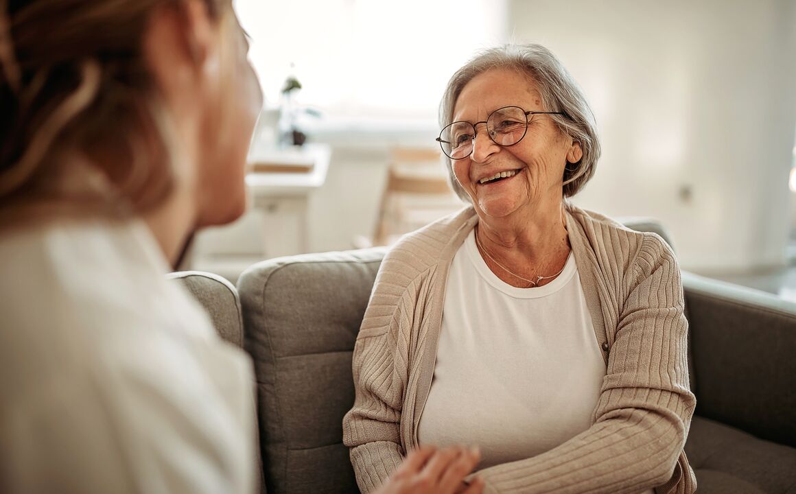 Clinical professional conducts an assessment while facing an older woman sitting on a couch.