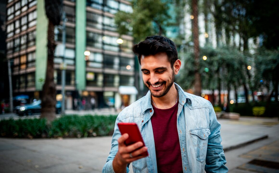 Young man checks the status of a government service transaction on his phone while standing outside an urban office building