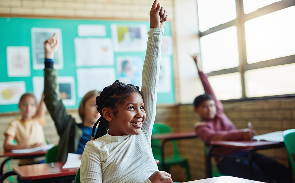 Image of children raising their hands while in a school classroom. 