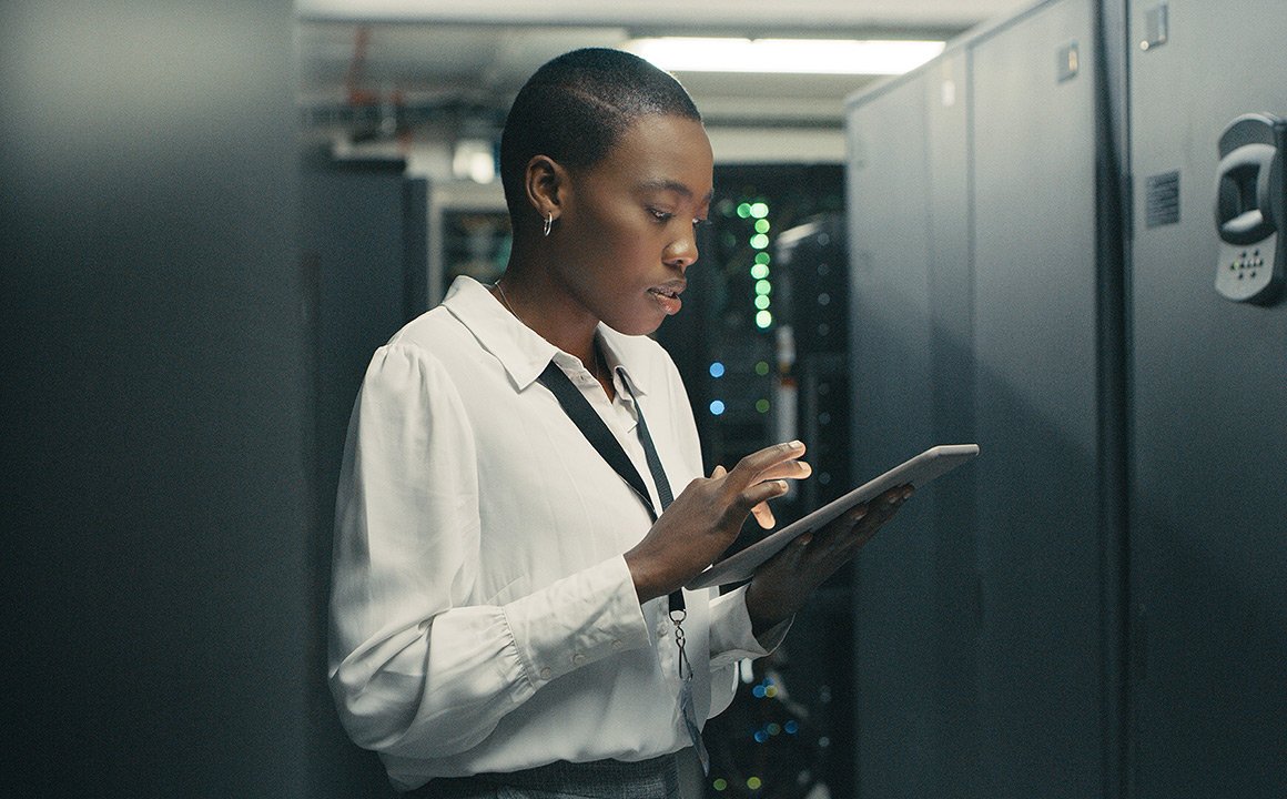 Image of a woman looking at a tablet while standing in a data center