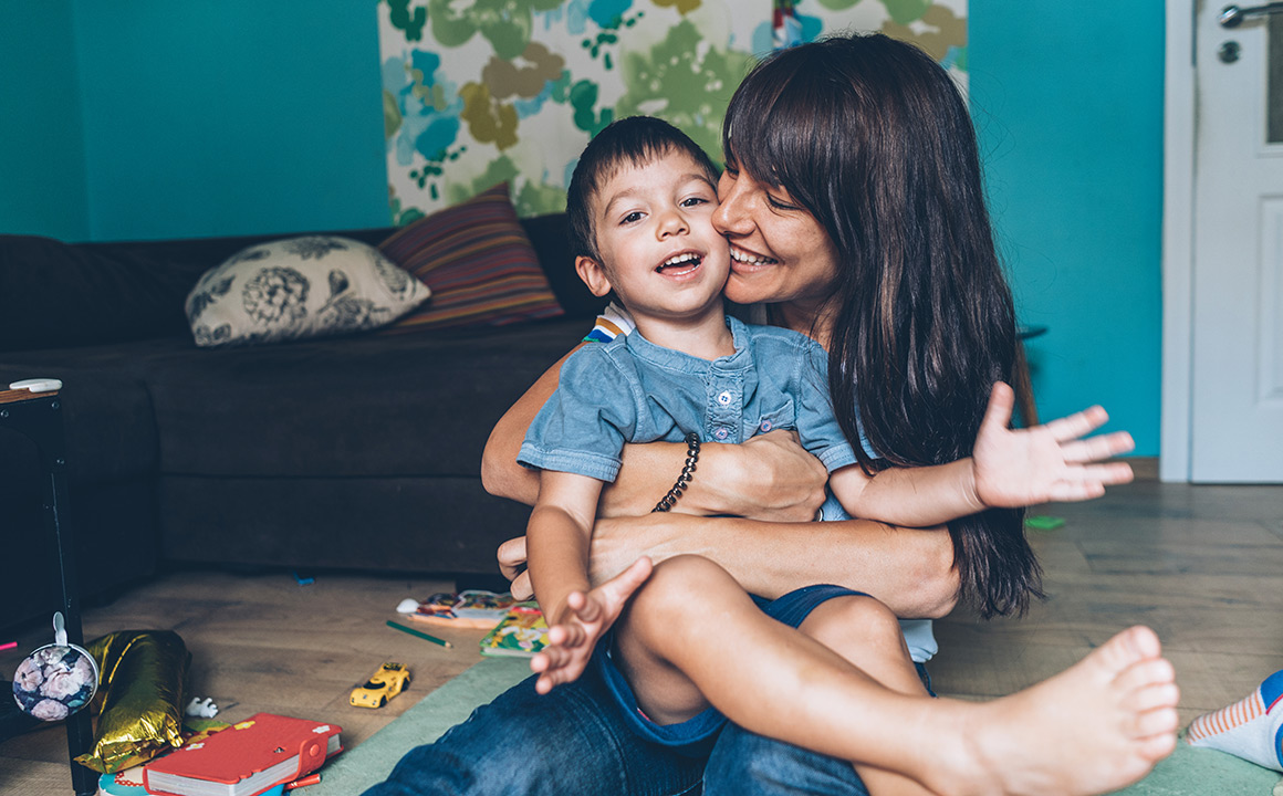Image of a woman holding her son on the floor smiling. 