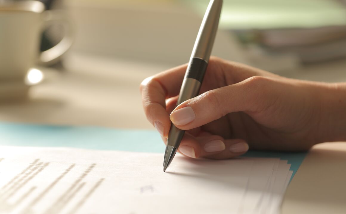 Image of a handing holding a pen while signing a document