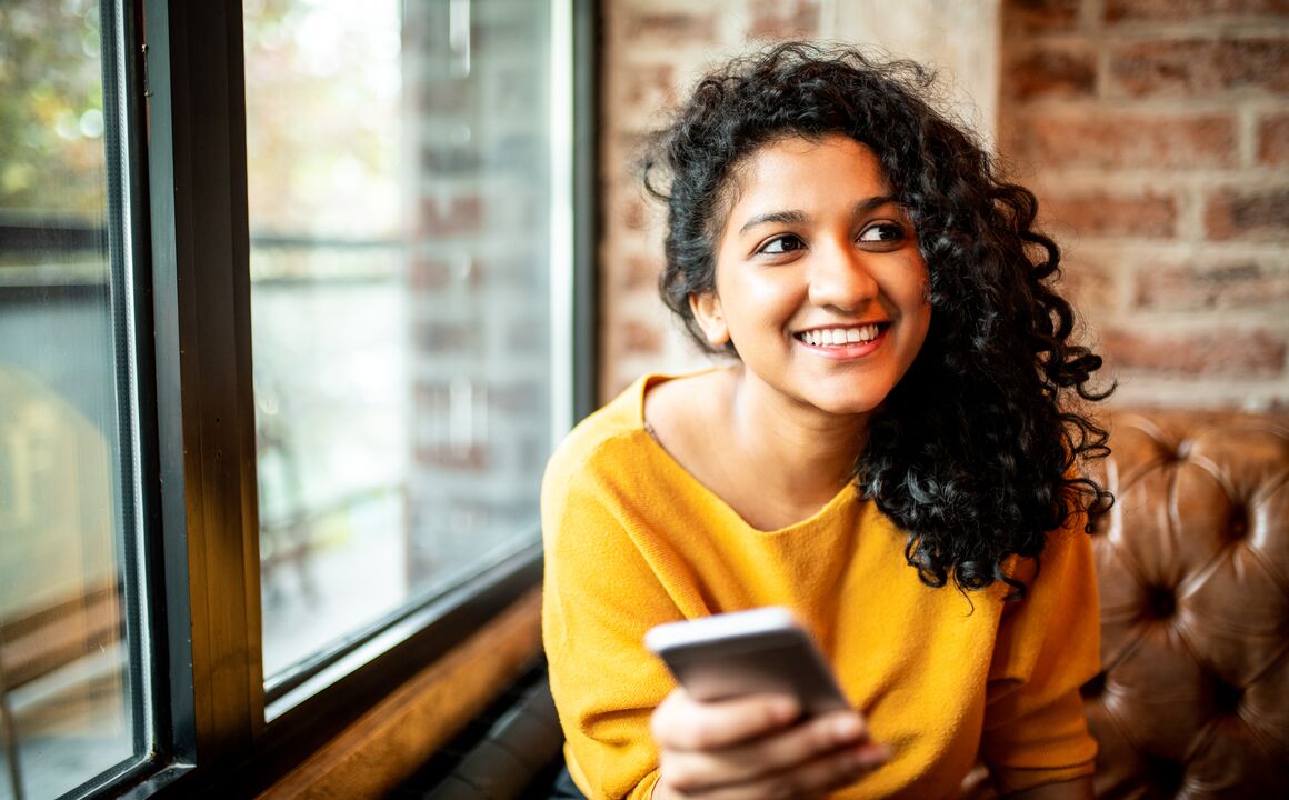 Image of a young woman smiling while holding her mobile device