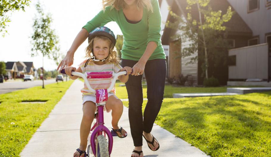 Image of a mother teaching her daughter how to ride a bike. 