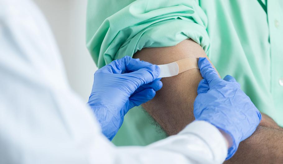 Image of health working applying band-aid to arm of patient.