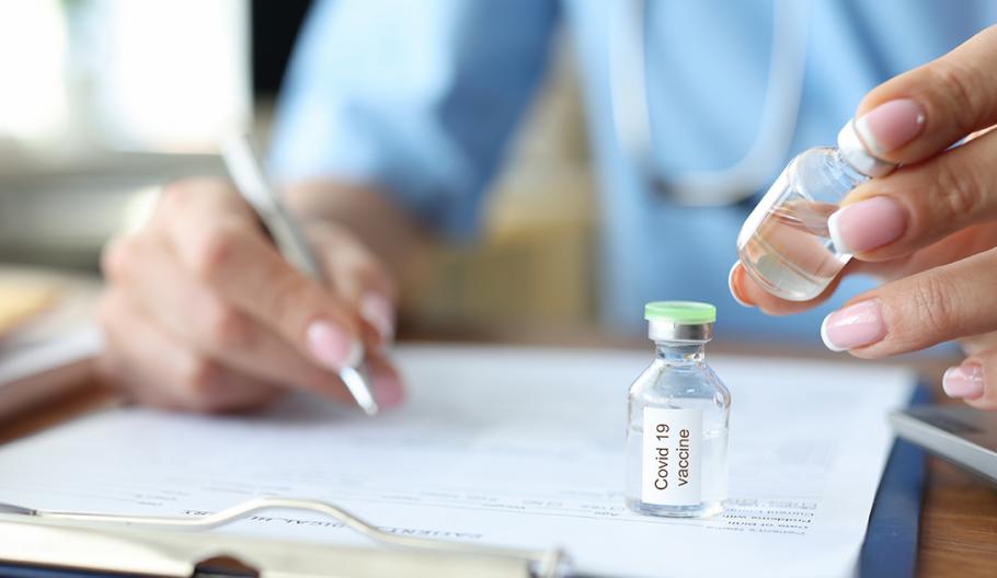Image of man writing with a vaccine vial on desk near him.