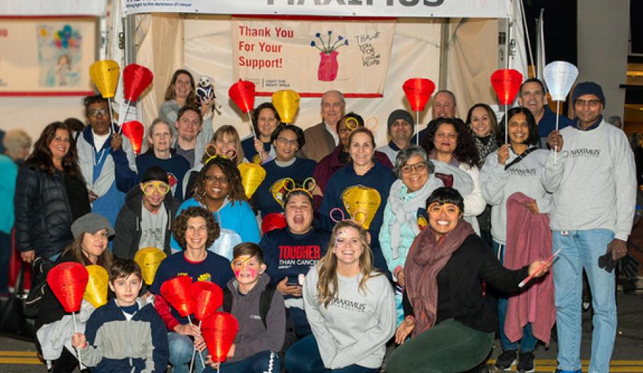 Image of Maximus employees, friends, and family members smile for a group photo. Many of them hold a lantern which signifies they are a supporter, survivor, or walking in memory of a loved one.