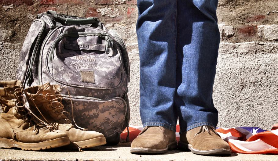 A person standing next to their military backpack, boots, and flag