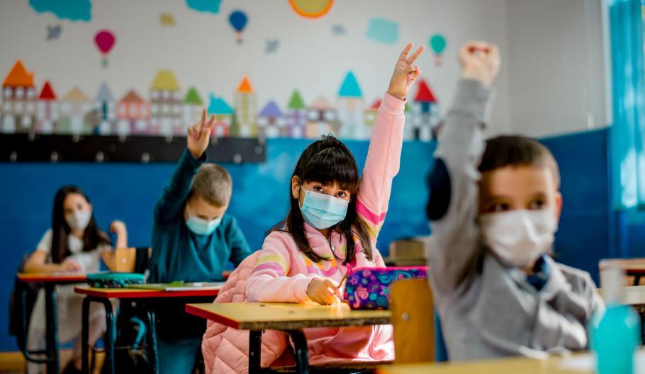 Image of a child raise her hand in class while wearing mask