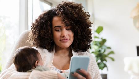 Image of a mother holding her child while looking at mobile device