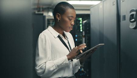 Image of a woman on her tablet while standing gin a server room