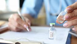 Image of man writing with a vaccine vial on desk near him.