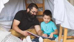 Image of a father and son in a blanket fort ready a book. 