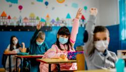 Image of a child raise her hand in class while wearing mask