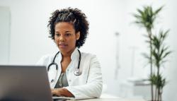 Image of a doctor sitting a her desk typing on her laptop