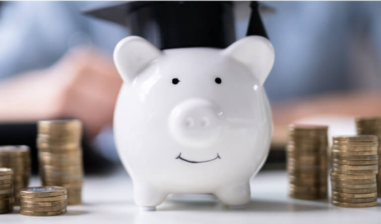 Pink bank wearing a graduation hat with a stack of coins off to both sides.