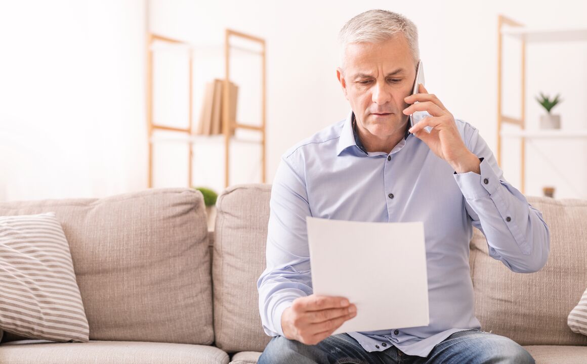 Image of an older man looking a piece of paper while on the phone